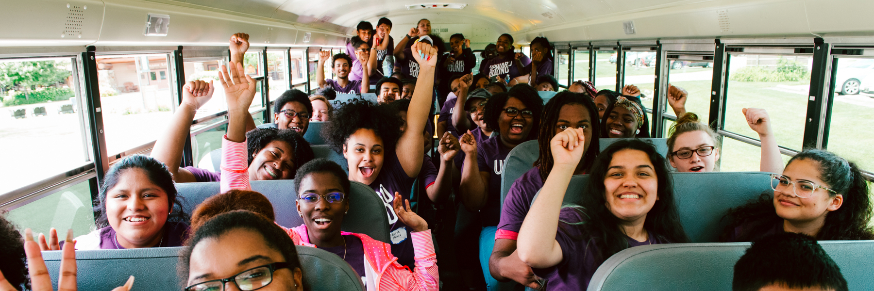 Upward Bound student smiling and raising their fists on a bus.